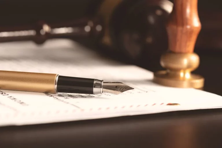 Penna stilografica dorata appoggiata su un documento, con un timbro in legno e ottone e un martelletto sullo sfondo scuro